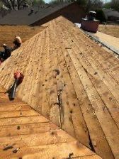 Workers on a rooftop with weathered wooden planks, likely preparing for a roofing project on a sunny day.