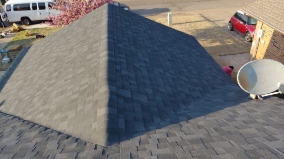 View of a dark gray roof with a pyramid shape. A white van and red car are visible in the background.