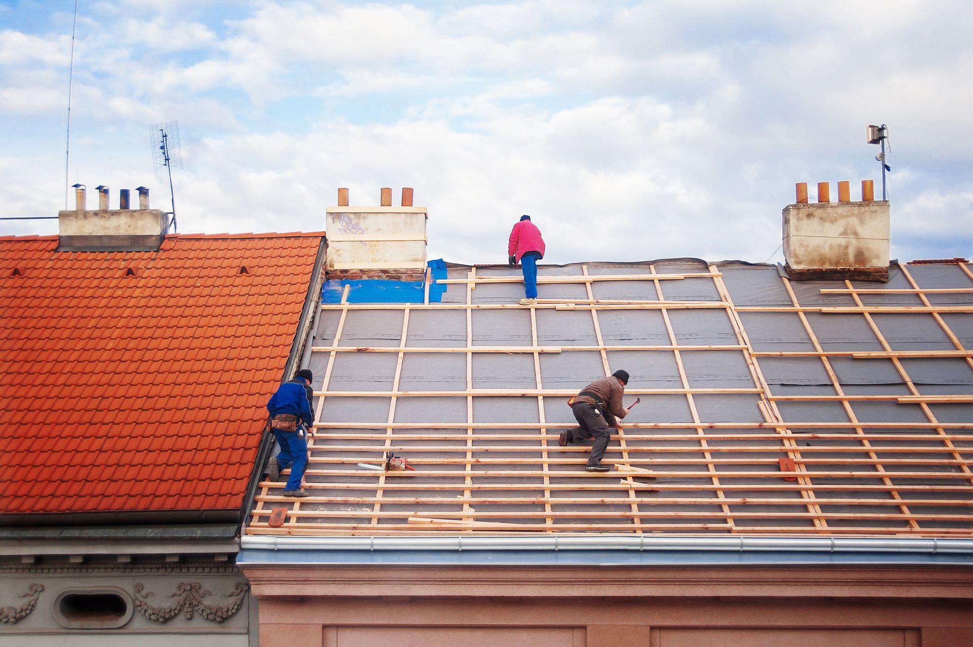 Workers performing roof replacement on a house, installing wooden battens across the rooftop safely 