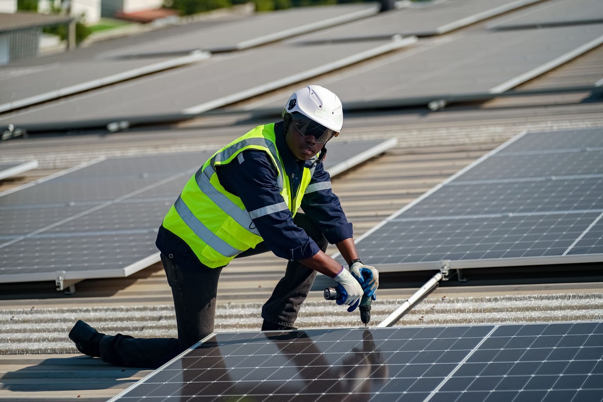 Worker installing solar panels on a rooftop, wearing a safety vest and helmet.
