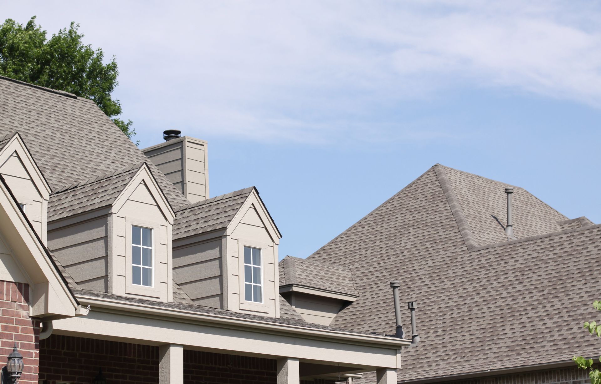 Gray asphalt shingle roof with gables, dormers, and a chimney on a residential home.