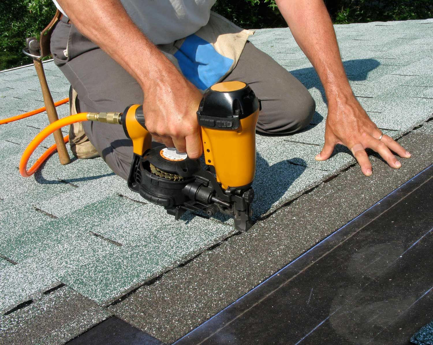 A roofer from a roofing contractor company, using a nail gun to apply asphalt shingles to a roof.