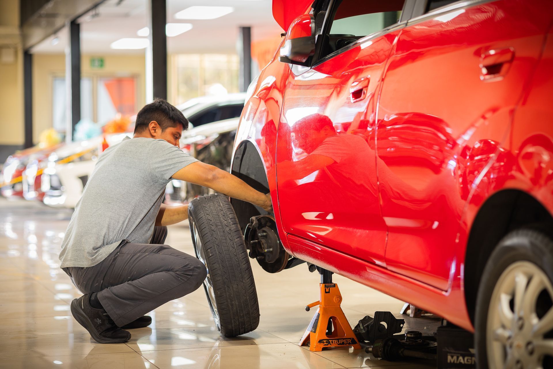 Un hombre está cambiando un neumático de un coche rojo en una sala de exposición.