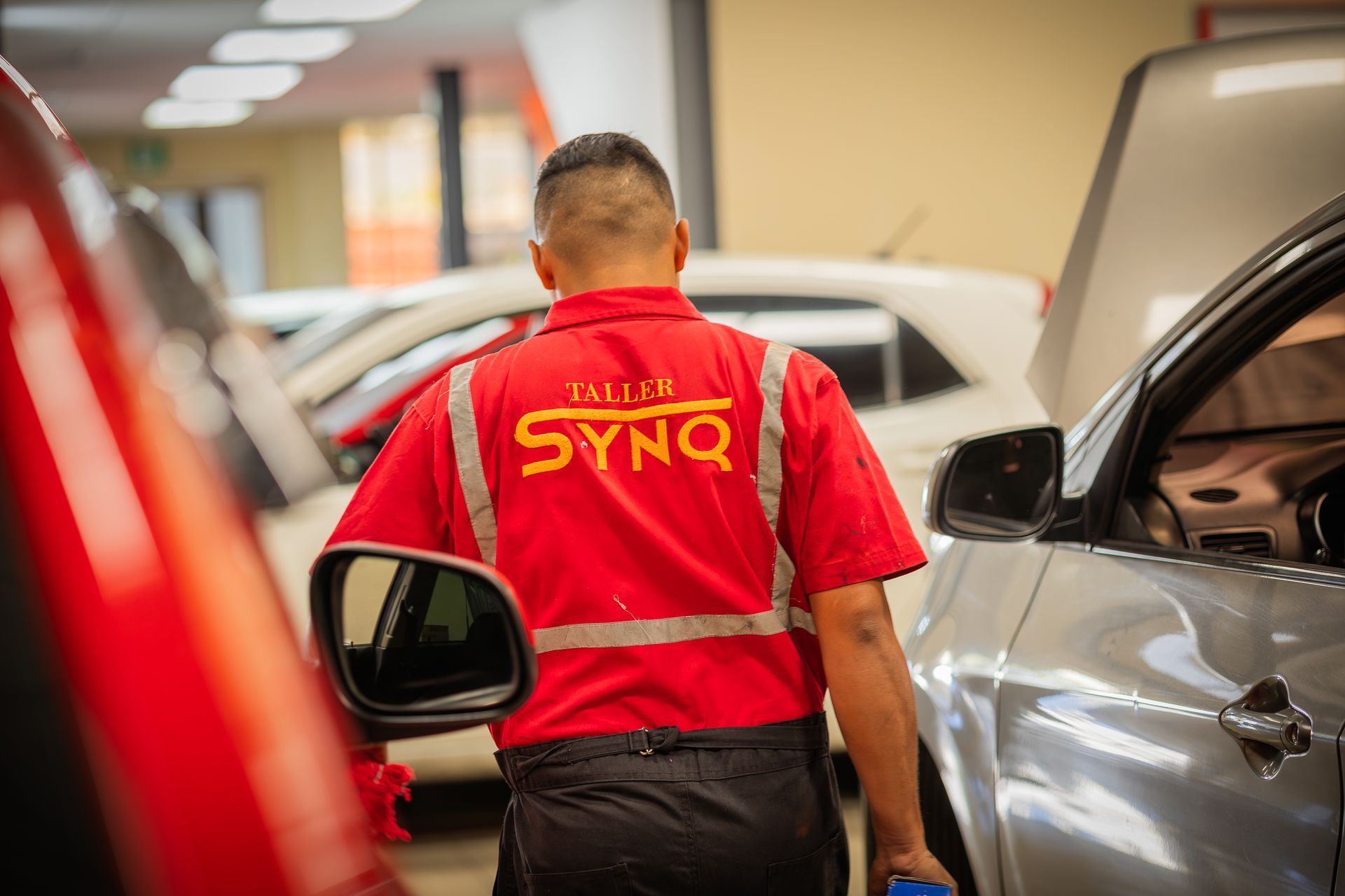 Un hombre con una camisa roja camina hacia un coche en un garaje.