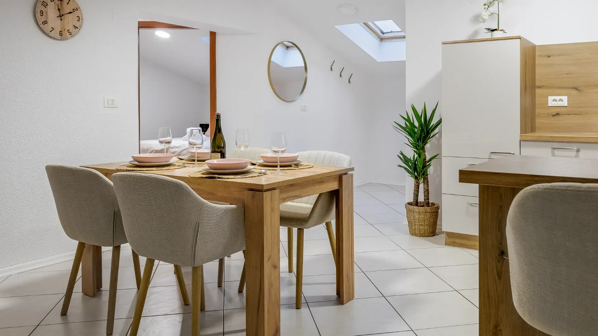 Dining area with wooden table set for a meal, neutral colored chairs, and a potted plant.