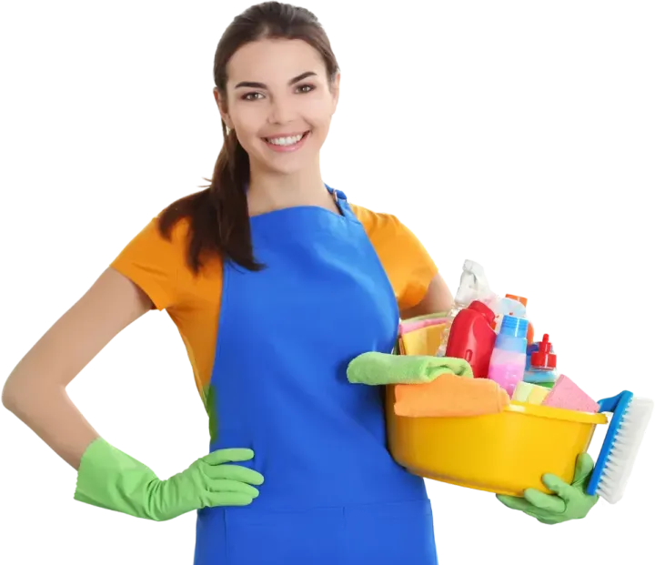 A smiling woman in a blue apron and green gloves holds a yellow cleaning supply caddy filled with bottles and cloths.