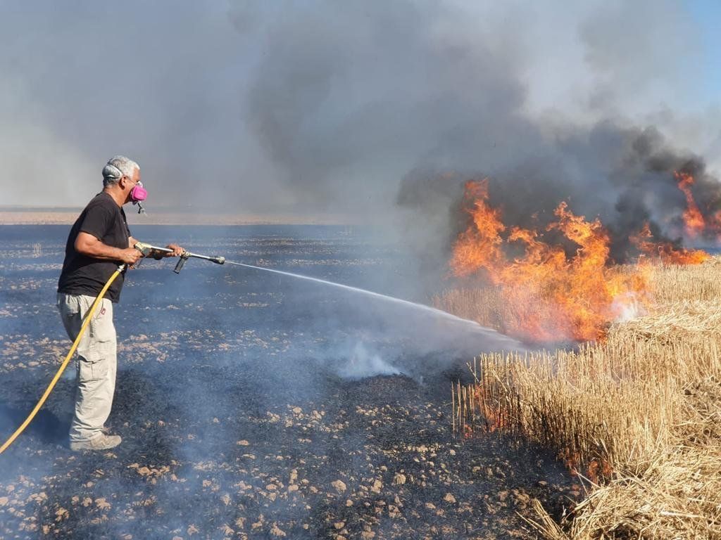 A man is spraying water on a fire in a field.