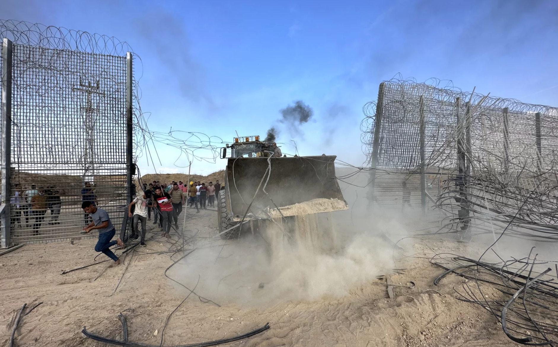 A bulldozer is destroying a barbed wire fence in the desert.