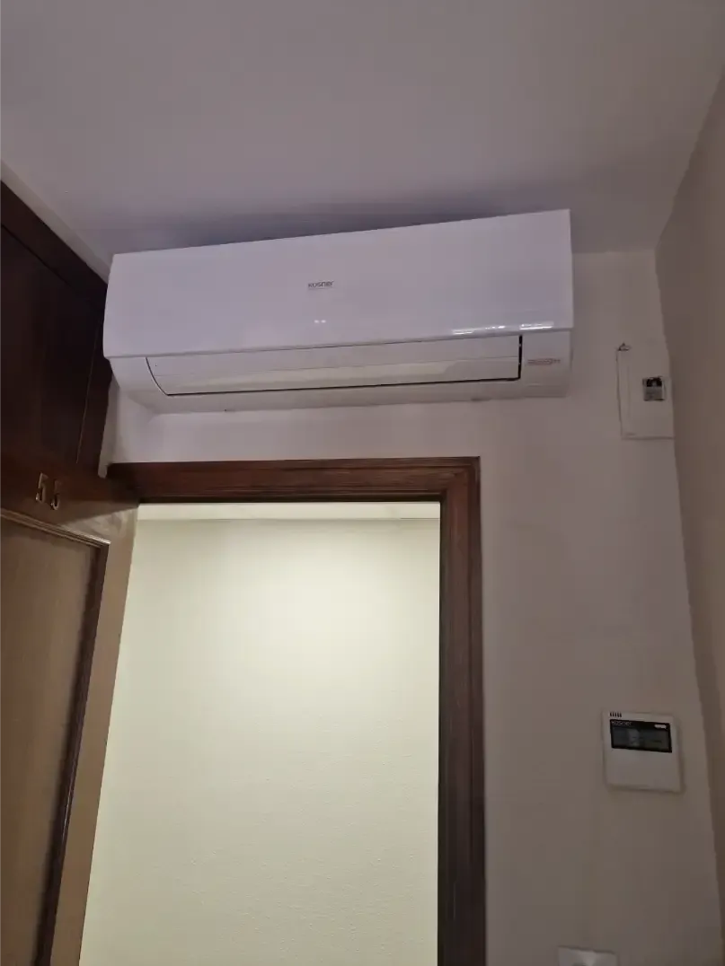 Aire acondicionado blanco montado en la pared sobre una puerta en una habitación beige.