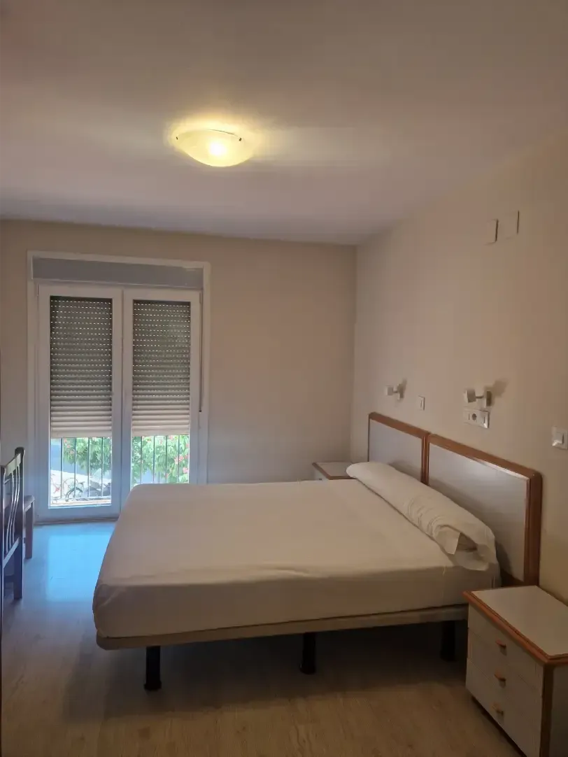 Habitación pequeña con cama, mesita de noche y ventana con persianas.