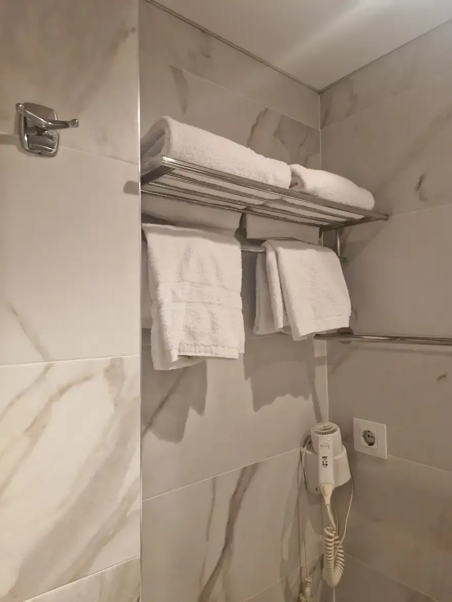 Estantería de baño con toallas enrolladas, toallas de mano colgantes y secador de pelo y enchufe montados en la pared.