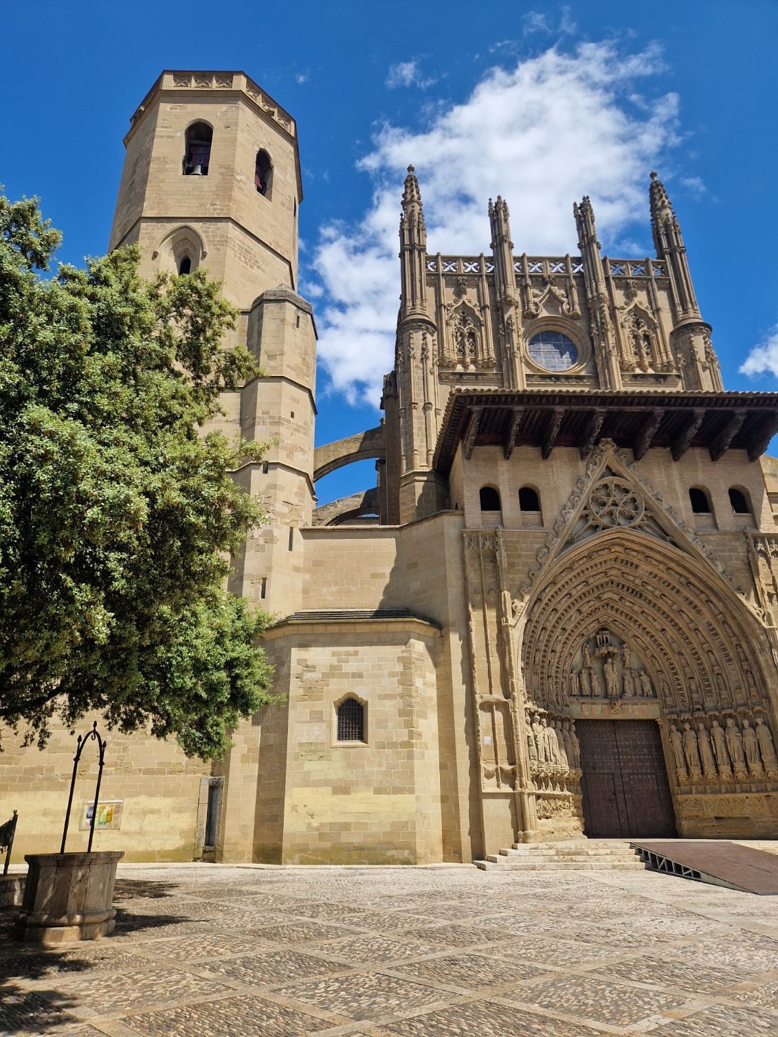 Catedral histórica de piedra con torre y fachada ornamentada bajo un cielo azul, vista desde un patio empedrado.