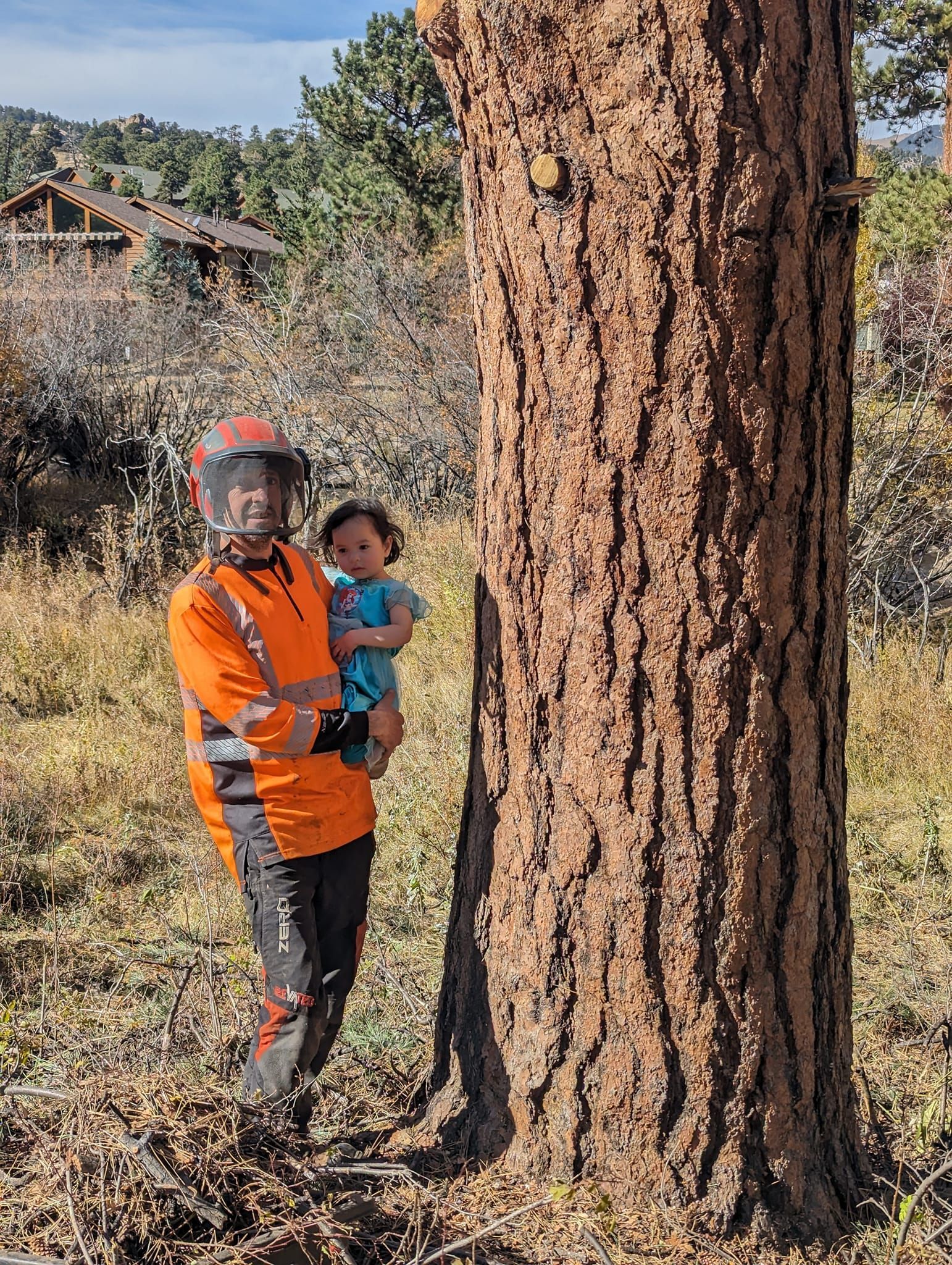 A man is holding a baby next to a tree.