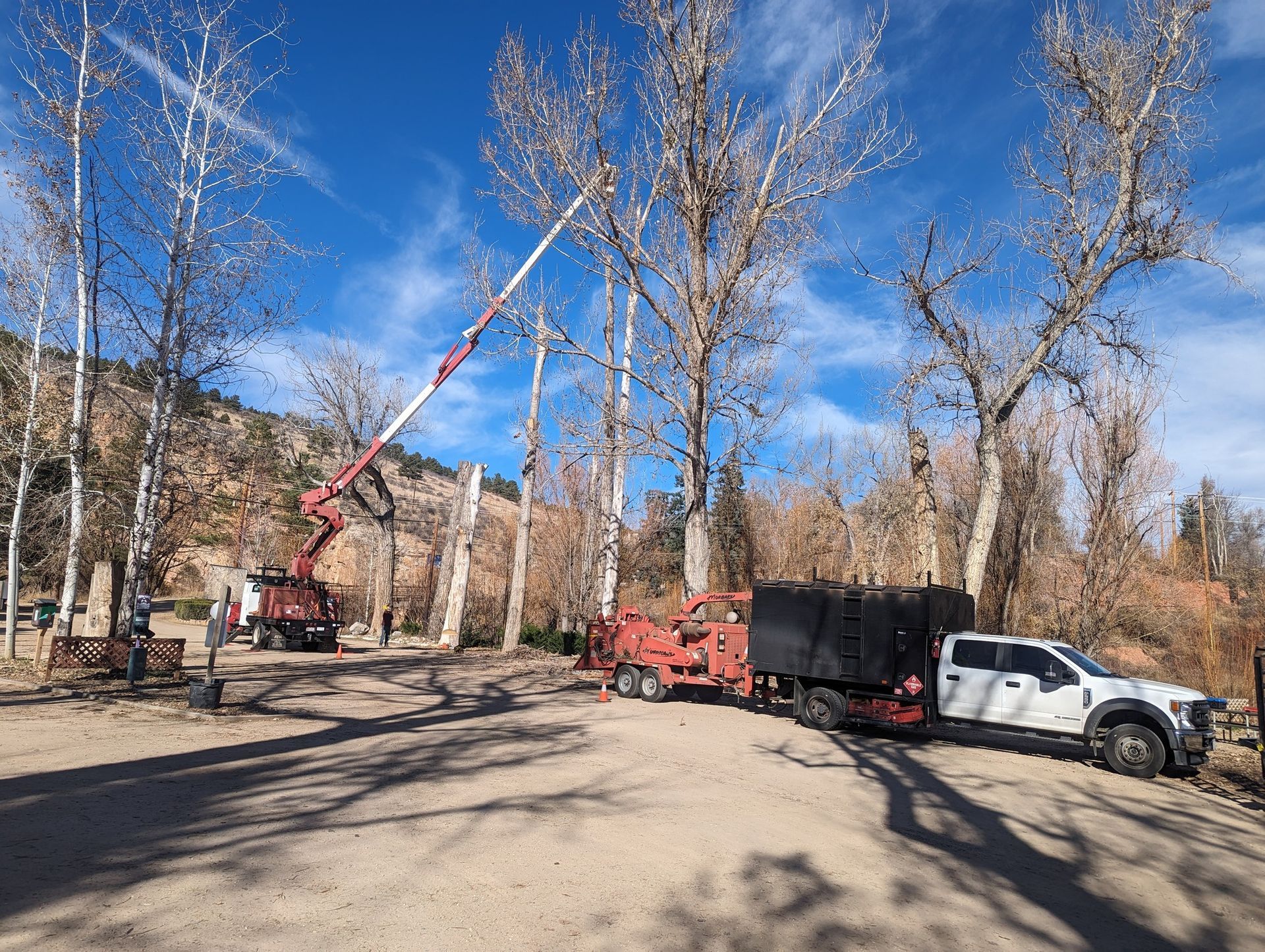 A white truck is parked in a dirt lot next to a tree cutting machine.
