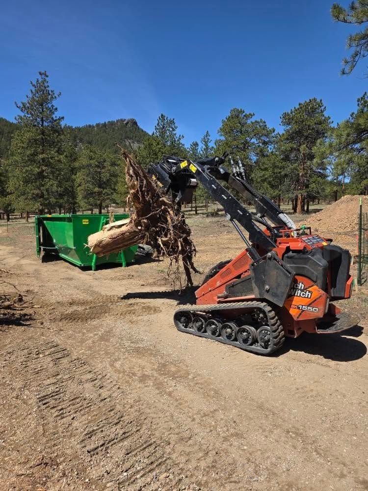 A bulldozer is carrying a large tree stump in a dirt field.