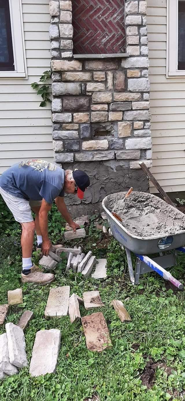 A man is working on a stone wall in front of a house.
