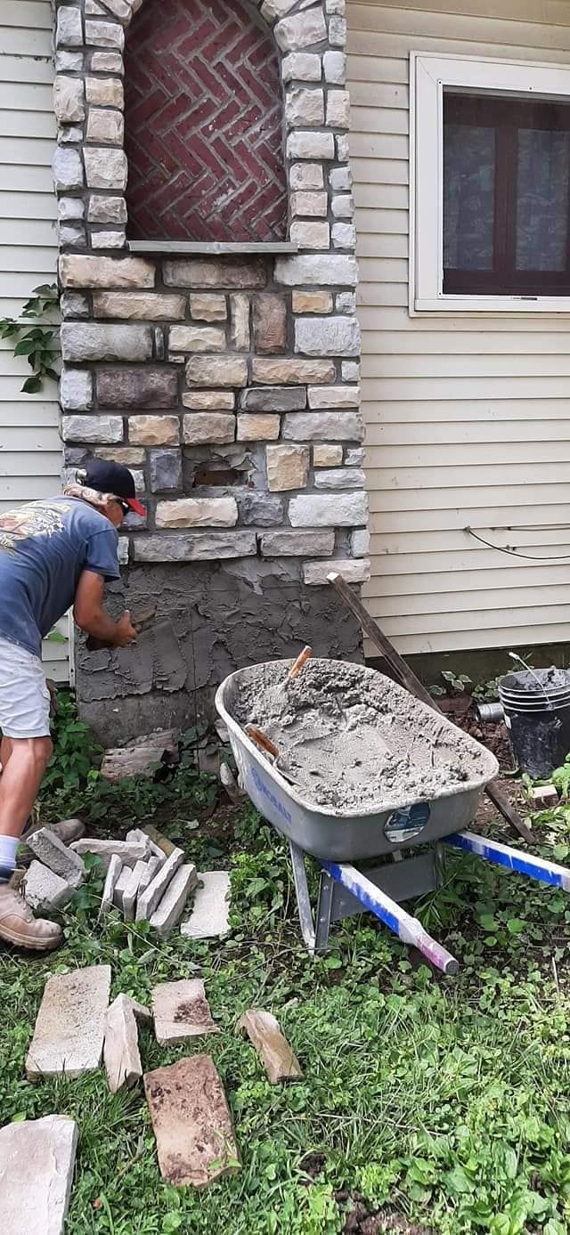 A man is working on a brick wall next to a wheelbarrow filled with cement.