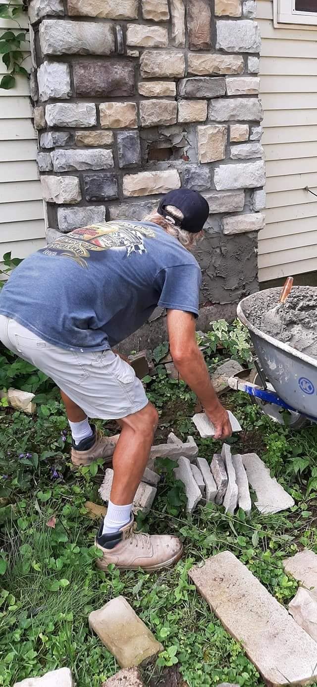 A man is working on a stone wall in front of a house.