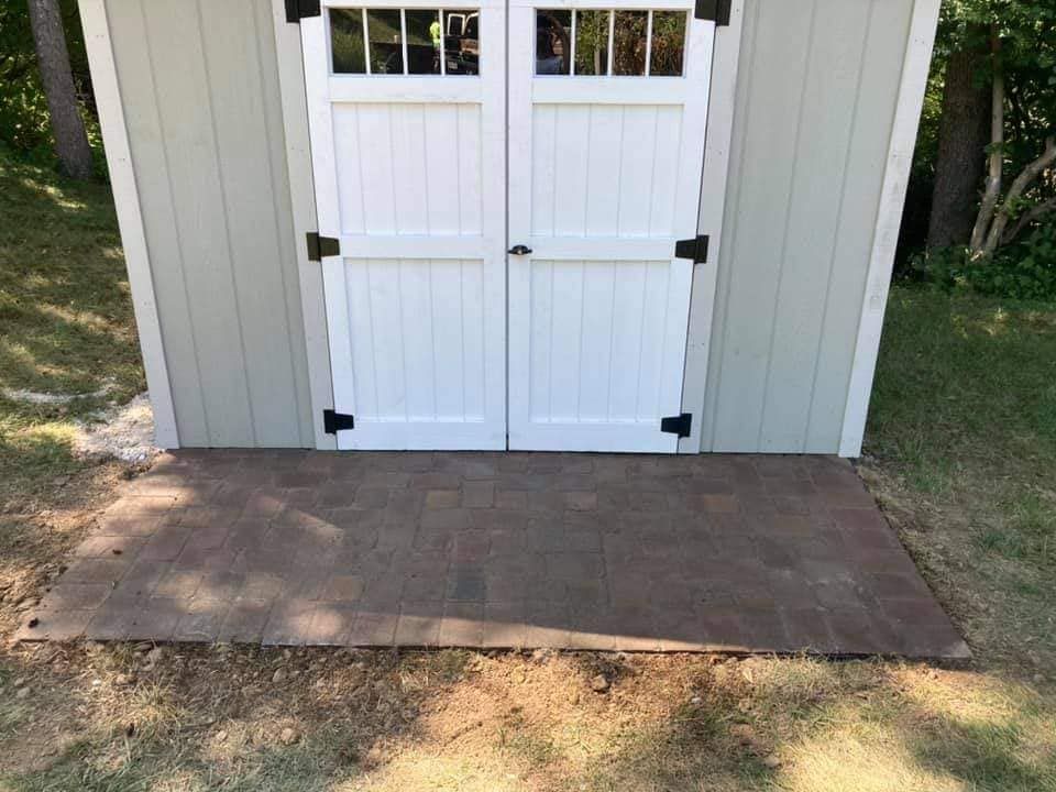 A shed with white doors and a concrete floor in front of it.