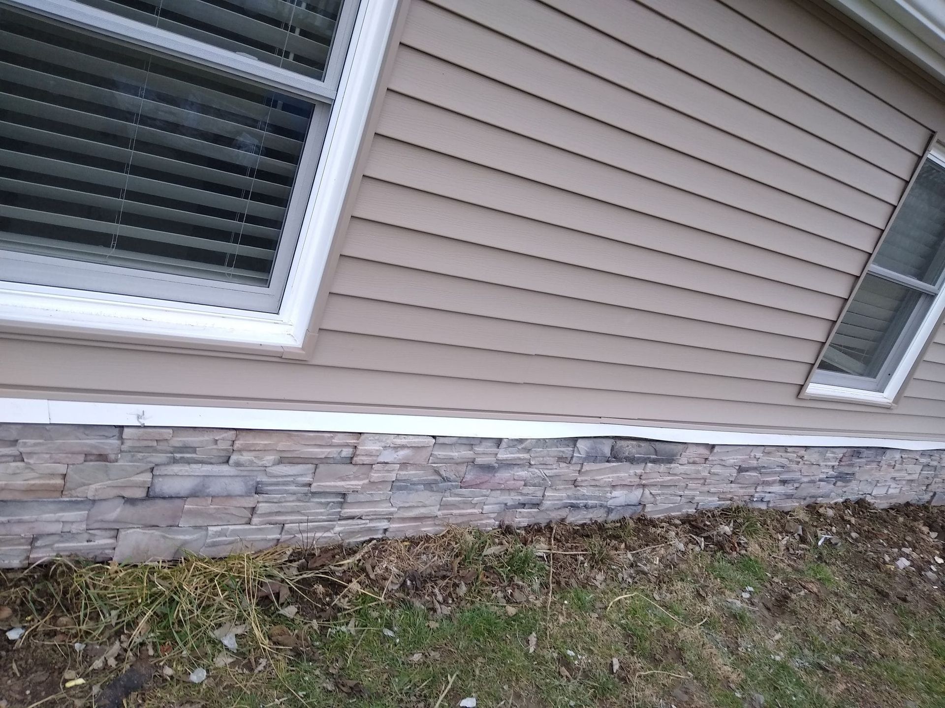 The side of a house with a window and a stone wall.