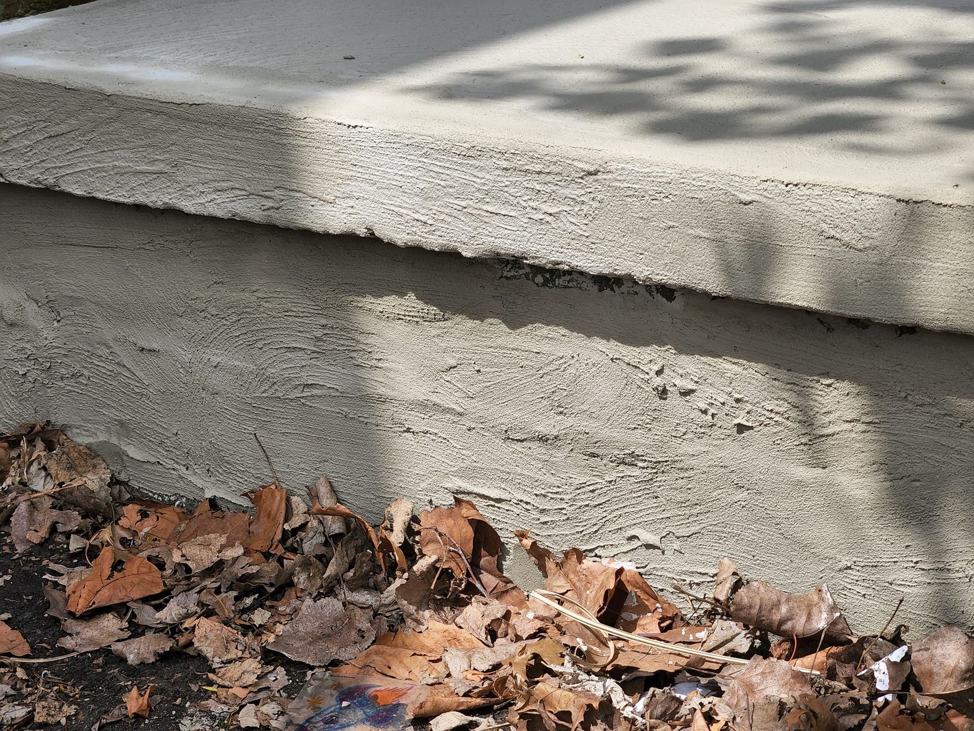 A concrete step with leaves on the ground next to it.