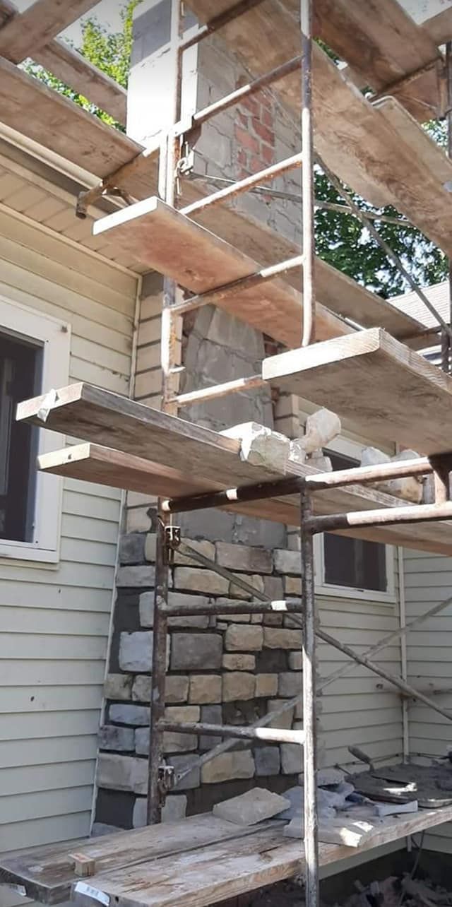 Scaffolding is being used to build a stone wall on the side of a house.