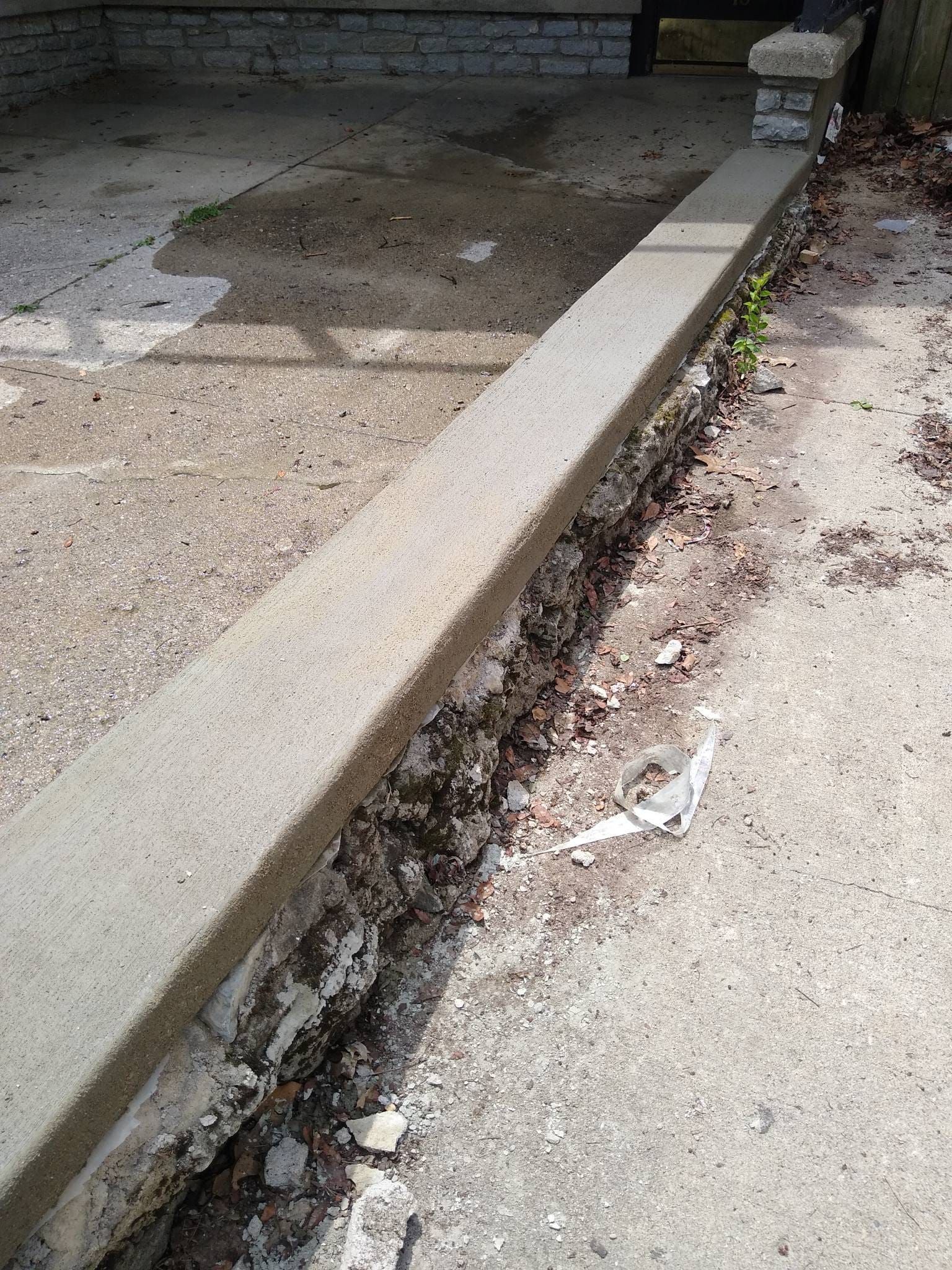 A close up of a concrete curb with a brick wall in the background.