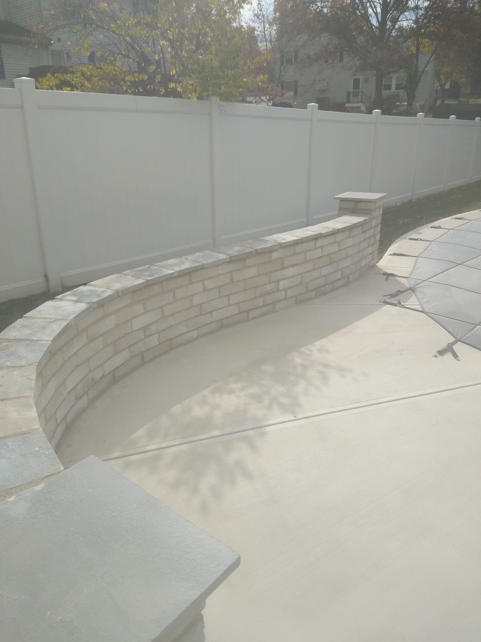 A white fence surrounds a patio with a curved brick wall.
