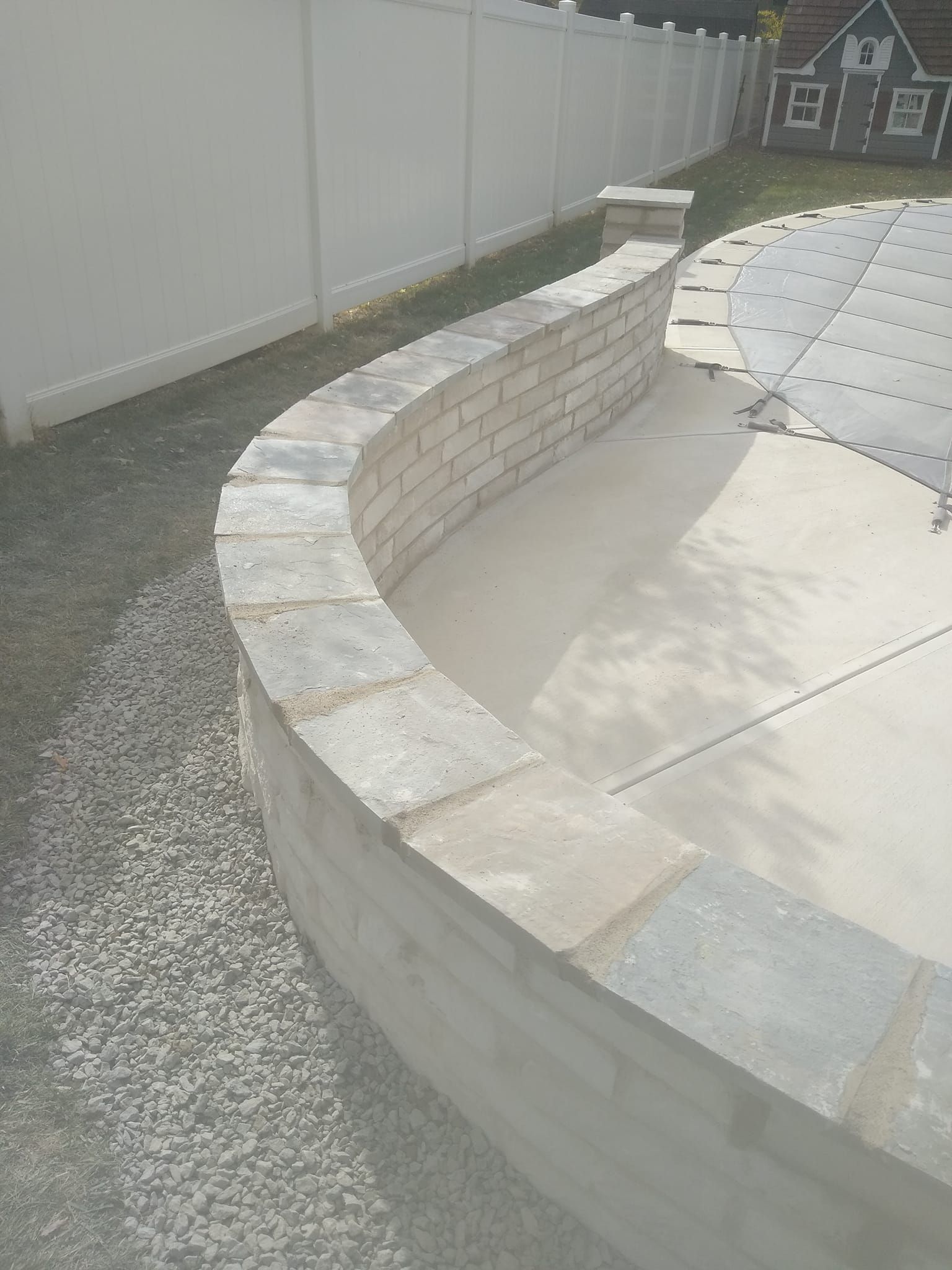 A brick wall surrounding a swimming pool with a white fence in the background.