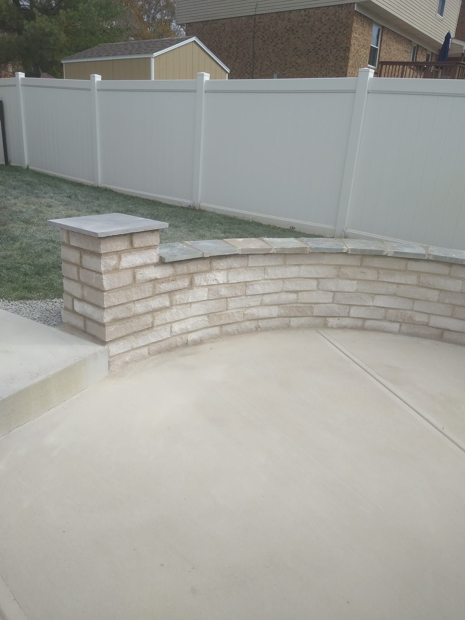 A brick wall with a white fence in the background