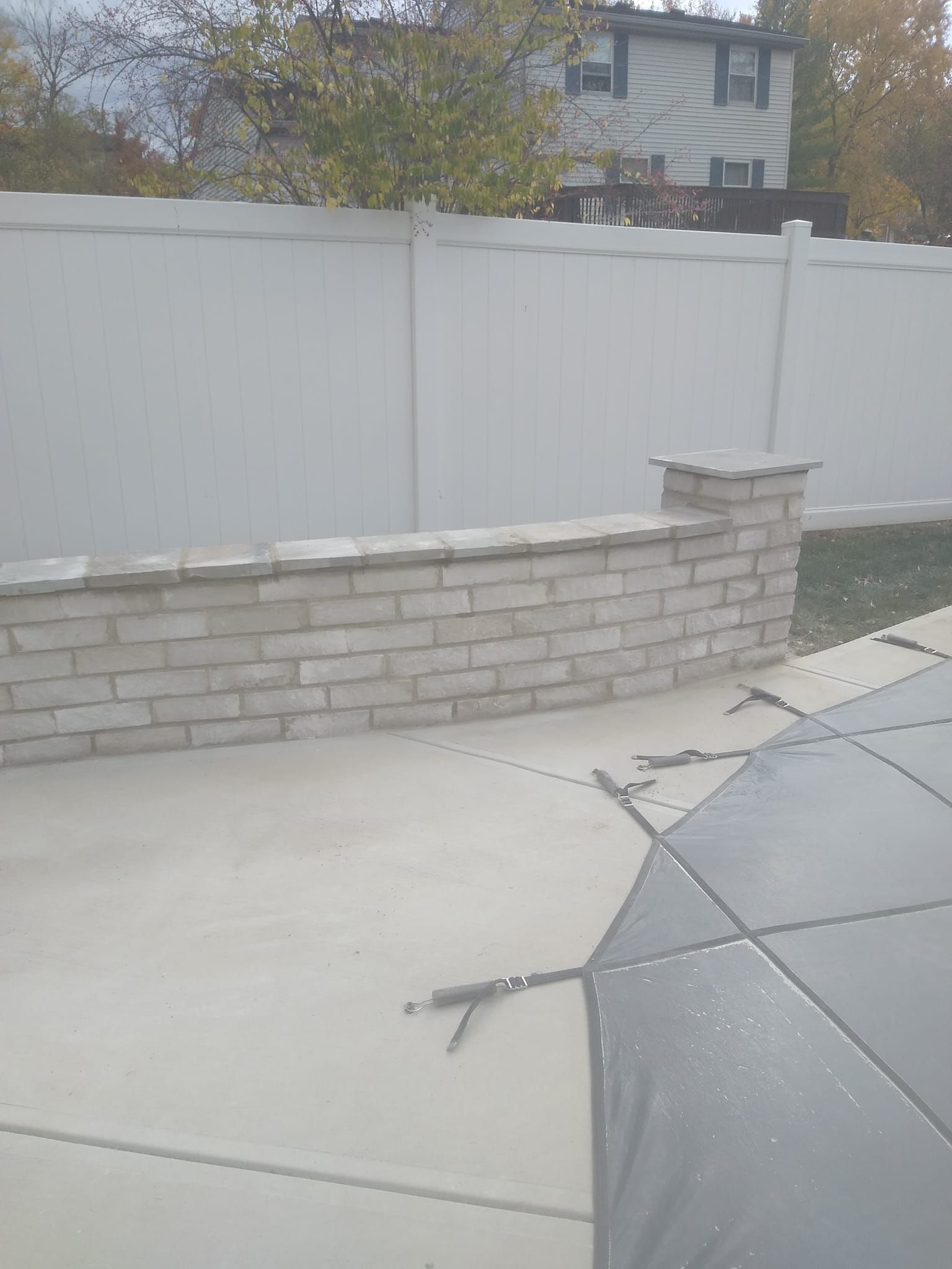 A brick wall next to a pool with a white fence in the background