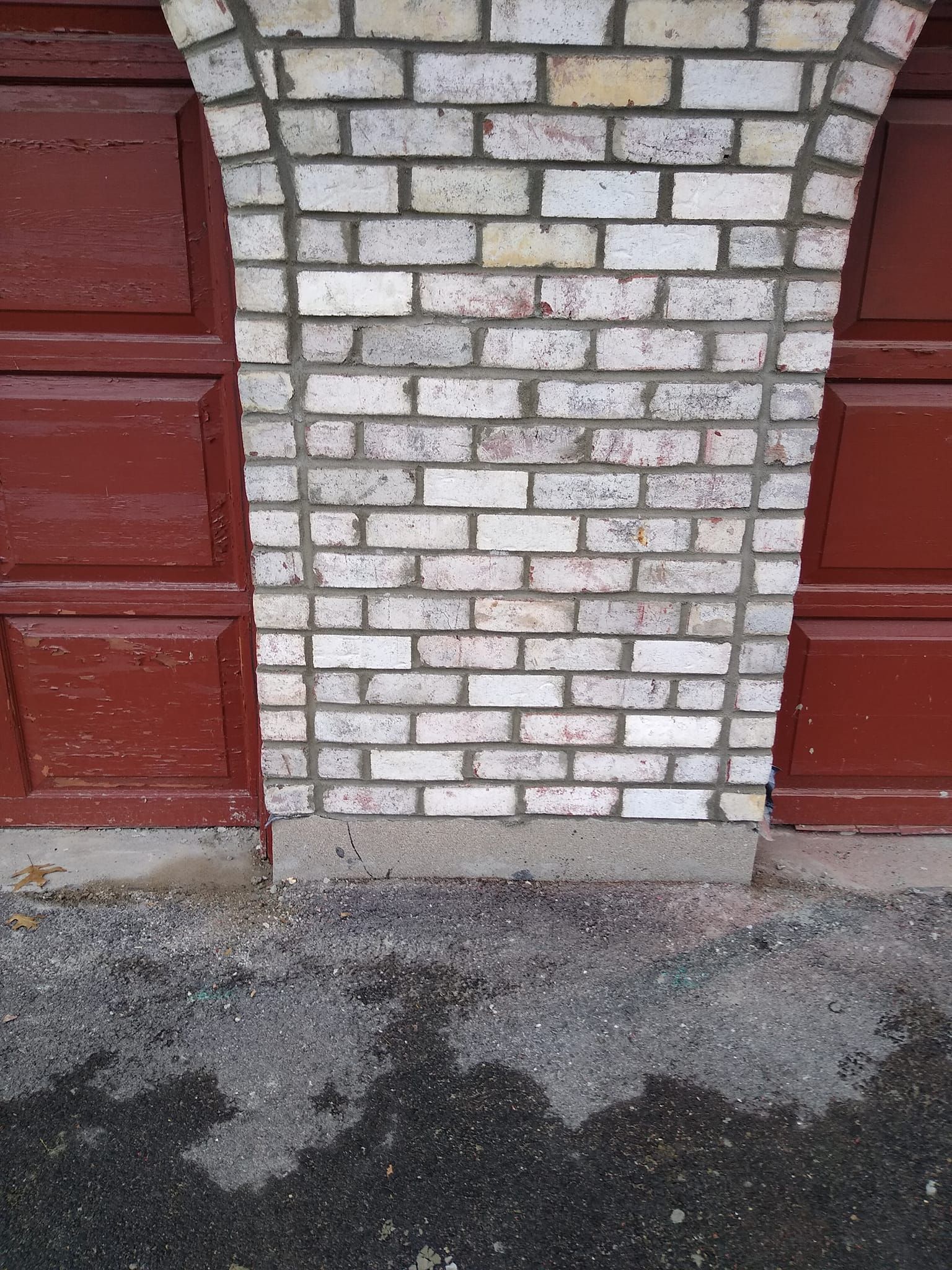 A brick wall with a red garage door in the background.