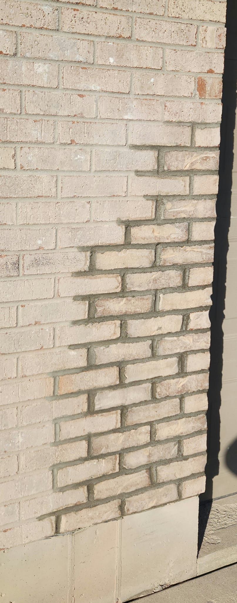 A white brick wall with a shadow on the sidewalk.