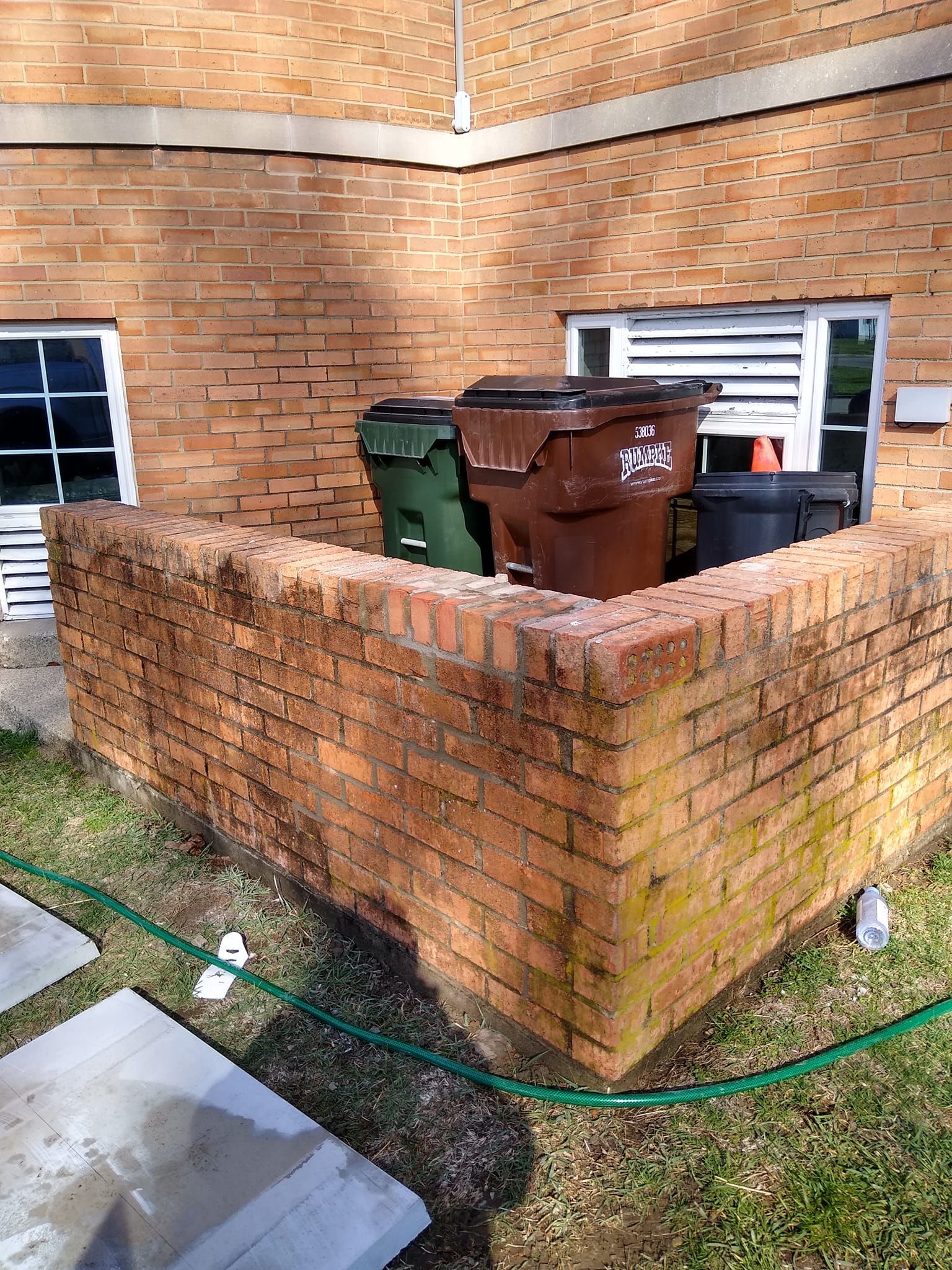 Three trash cans are sitting on a brick wall next to a window.