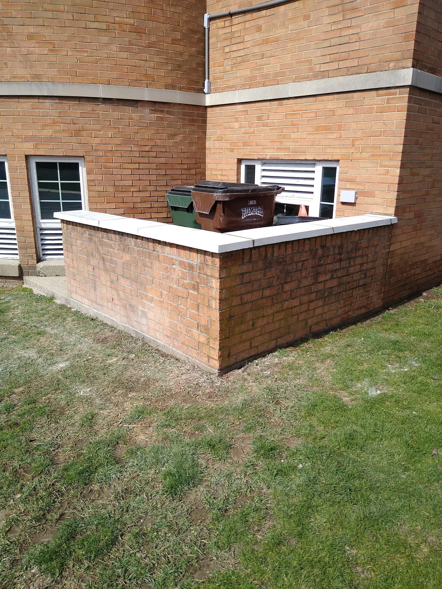 A brick wall with trash cans on it in front of a brick building.
