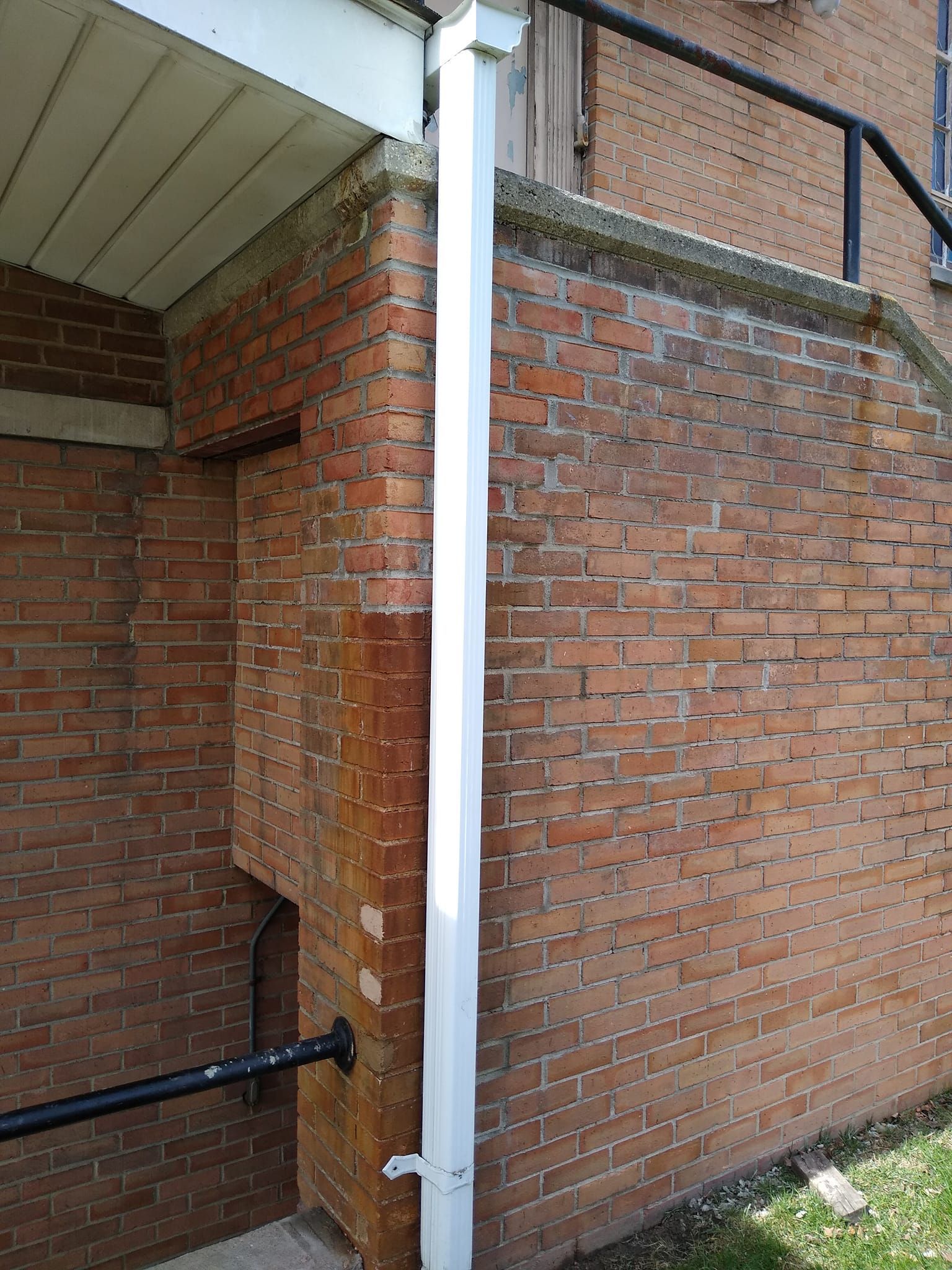 A white gutter is attached to the side of a brick building.