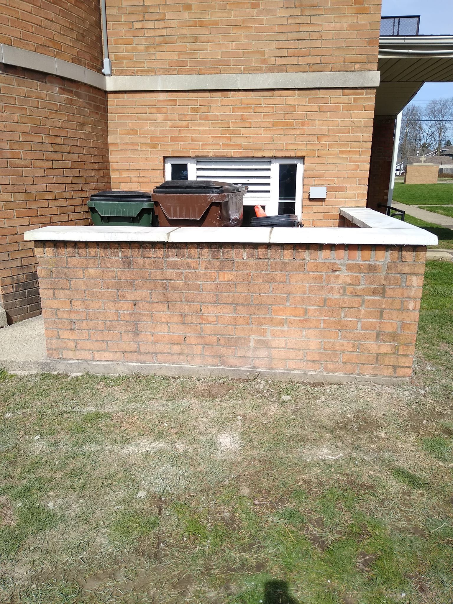 A brick wall with trash cans in front of a brick building.