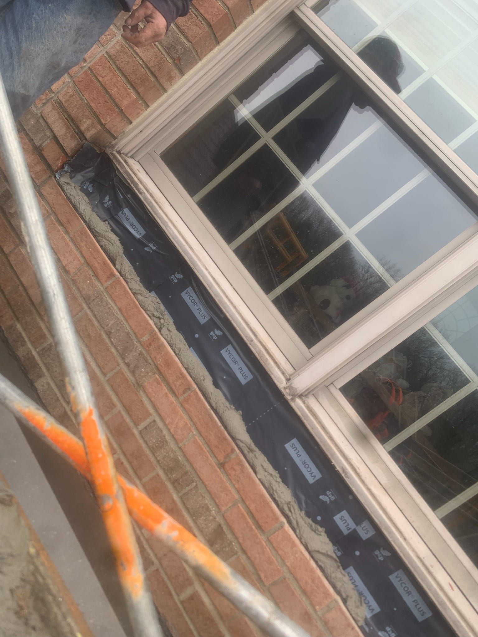 A man is standing on a scaffolding next to a window on a brick wall.