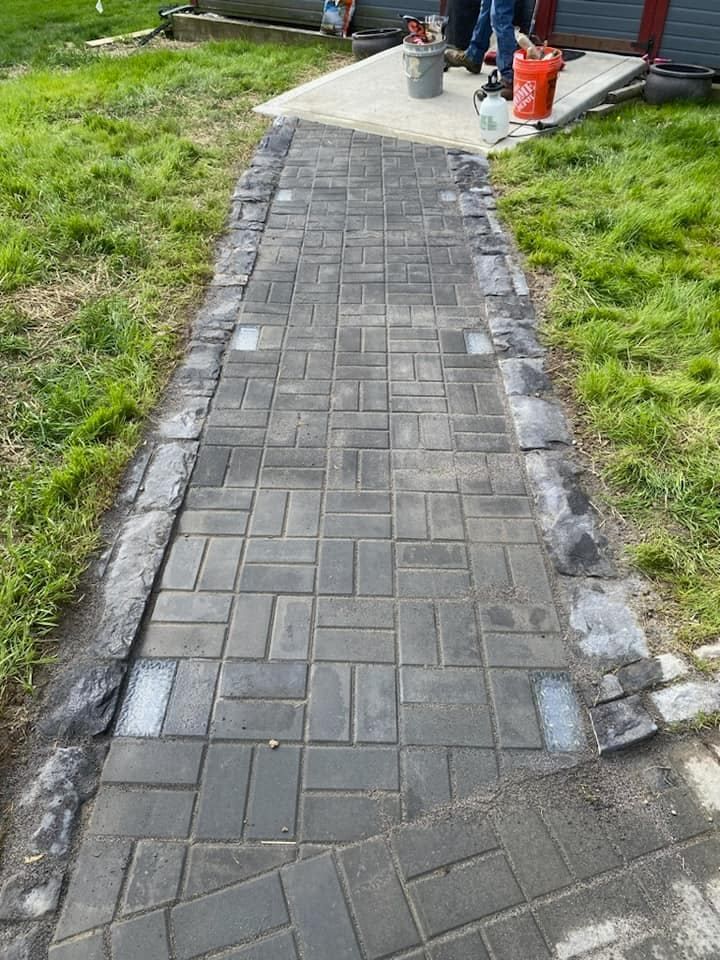 A brick walkway is being painted in a yard.
