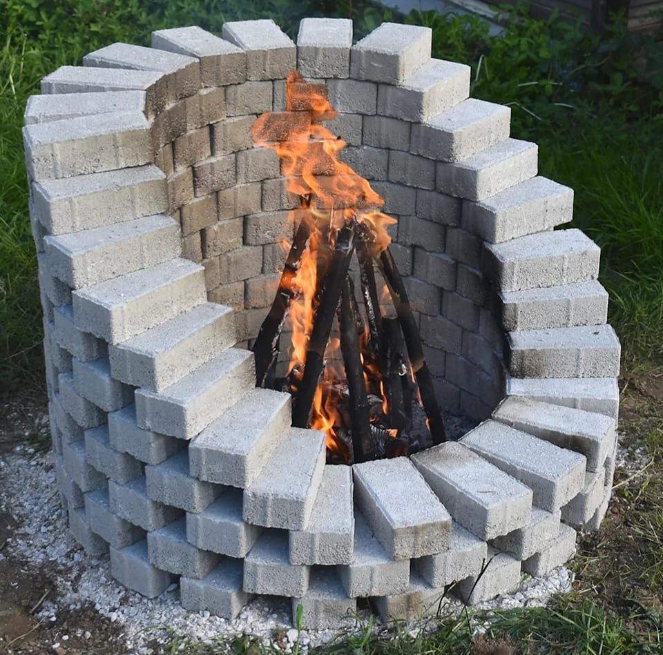 A fire pit made out of bricks is surrounded by grass
