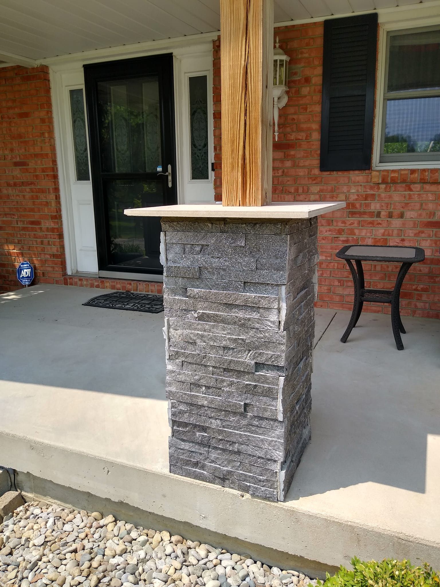 A stone column is sitting on a porch in front of a brick house.