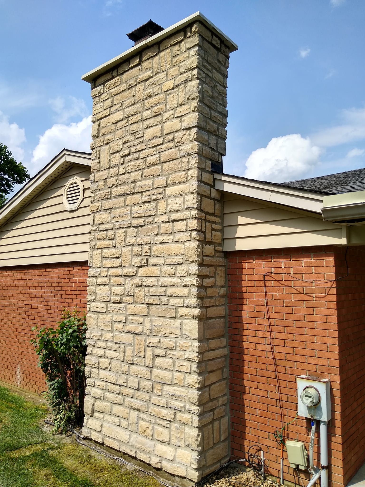 A large stone chimney is sitting on the side of a brick house.