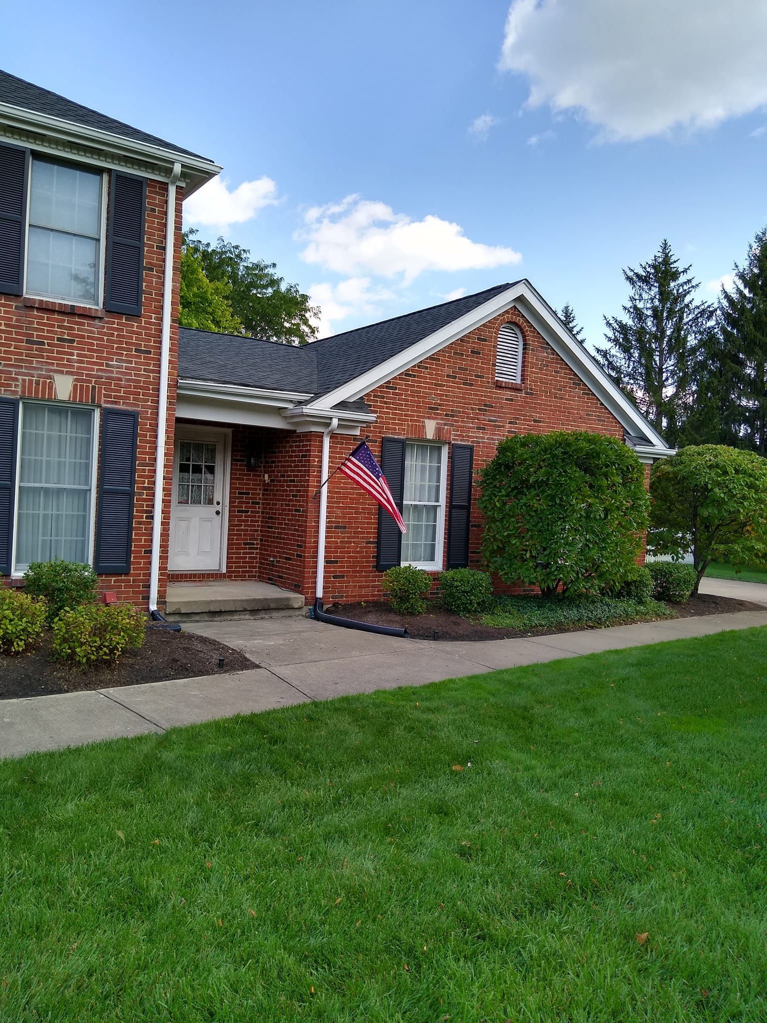 A brick house with black shutters and an american flag in front of it.