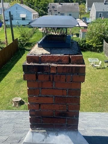 A brick chimney is sitting on top of a roof in a backyard.