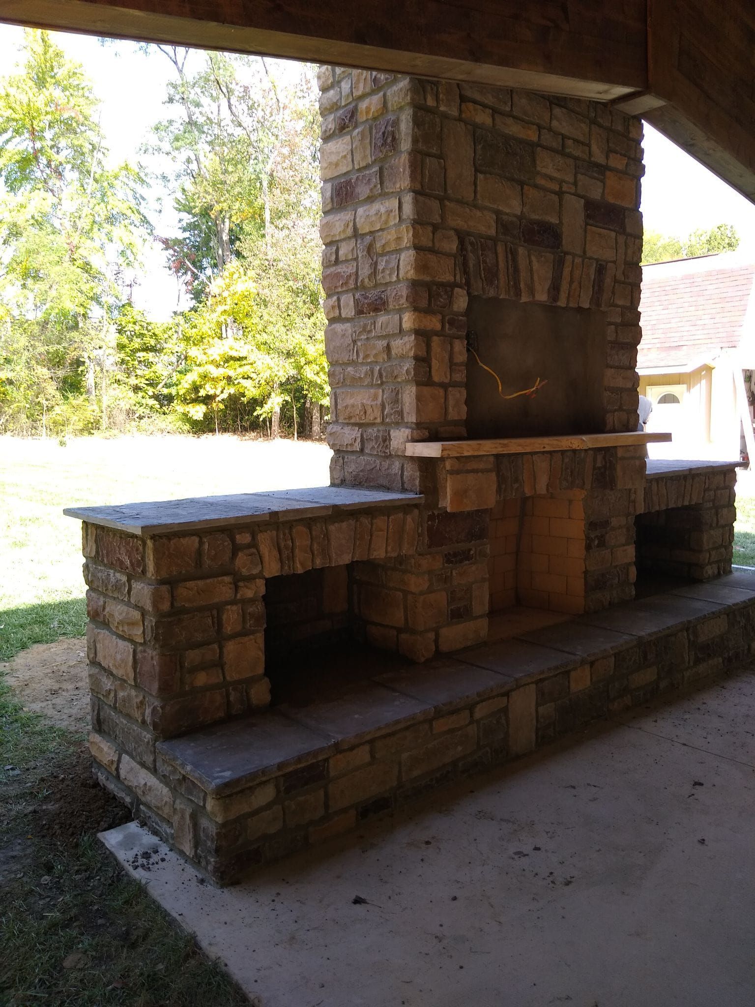 A stone fireplace is sitting under a covered patio.