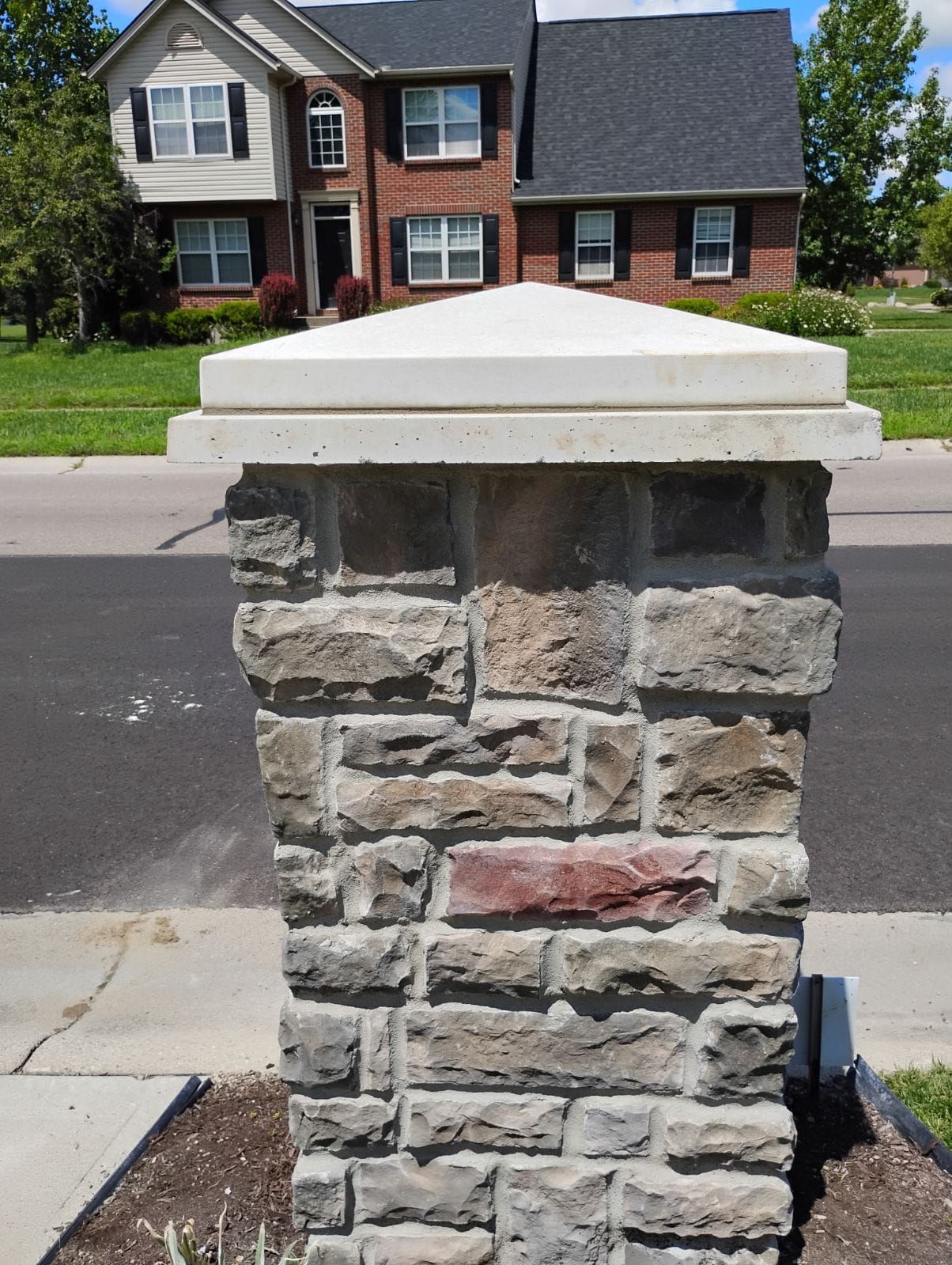 A stone post in front of a brick house