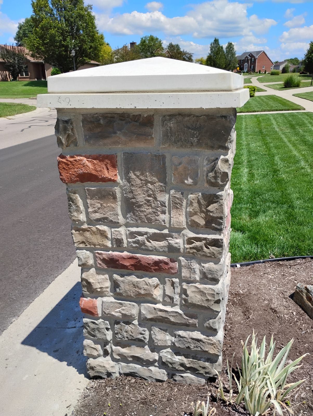 A stone pillar with a white top is sitting next to a lush green lawn.