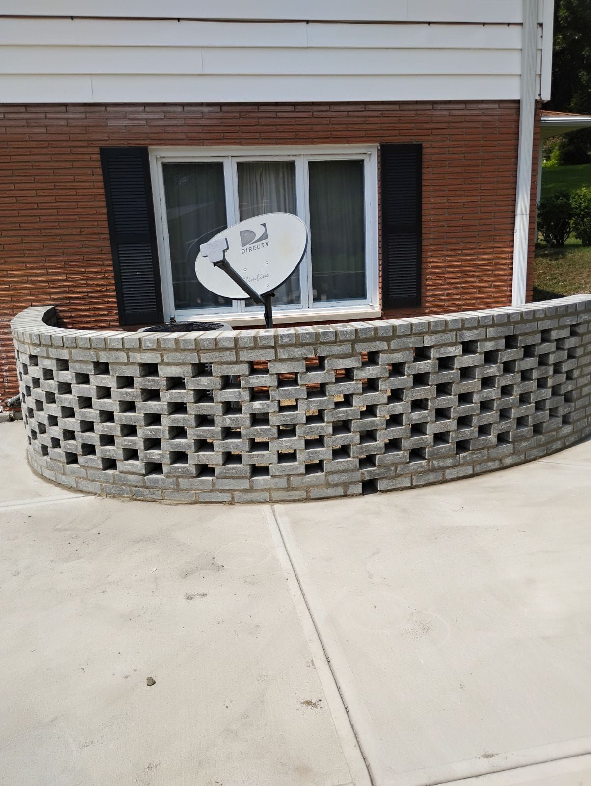 A brick wall with a satellite dish in front of a window.