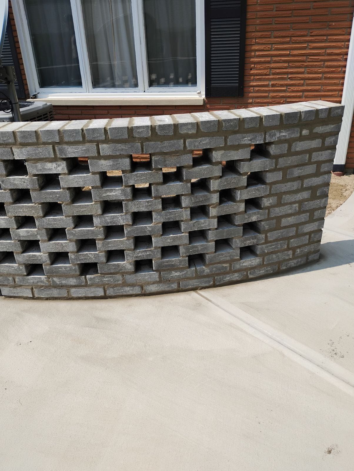 A brick wall is sitting on the sidewalk in front of a brick house.
