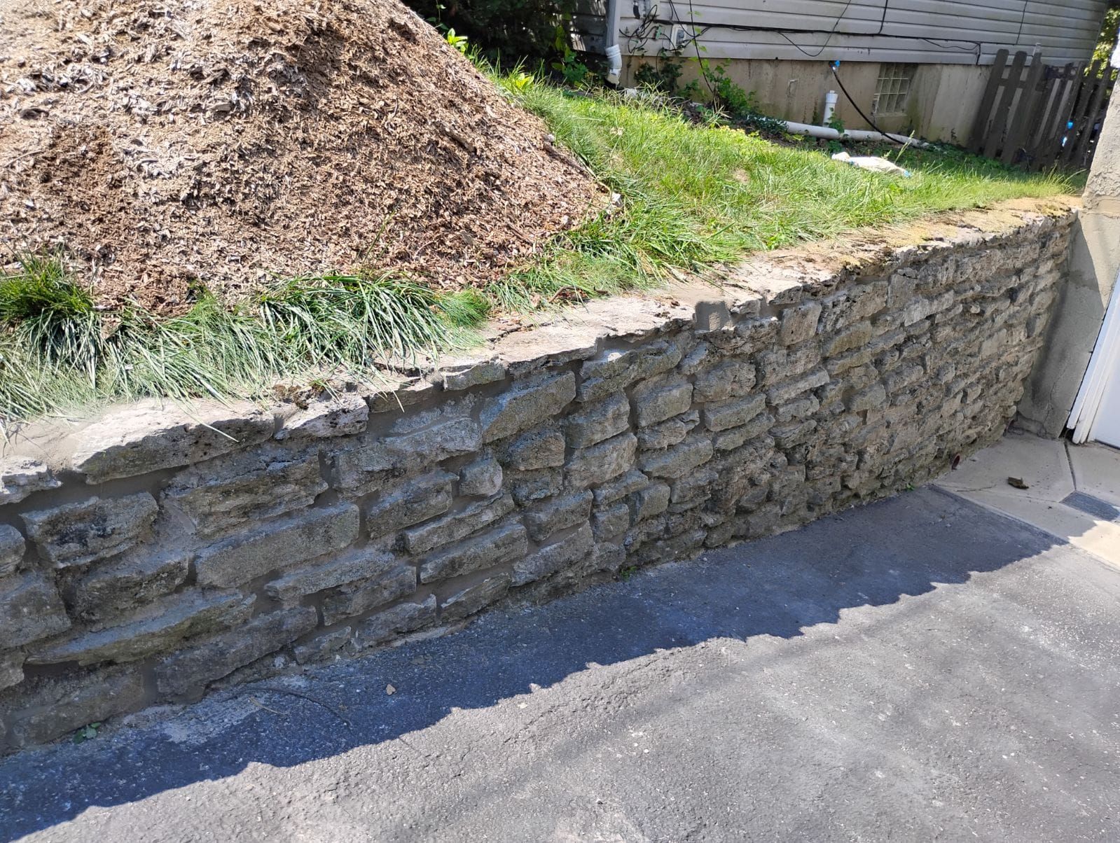 A stone wall is sitting on the side of a road next to a pile of dirt.